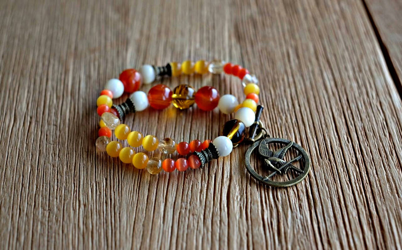 Orange- and golden-hued cat's eye, agate, manmade and natural citrine as well as seawater Mother of Pearl beads in varying sizes make up this Muse, to represent the fiery flames accompanying the Mockingjay charm.