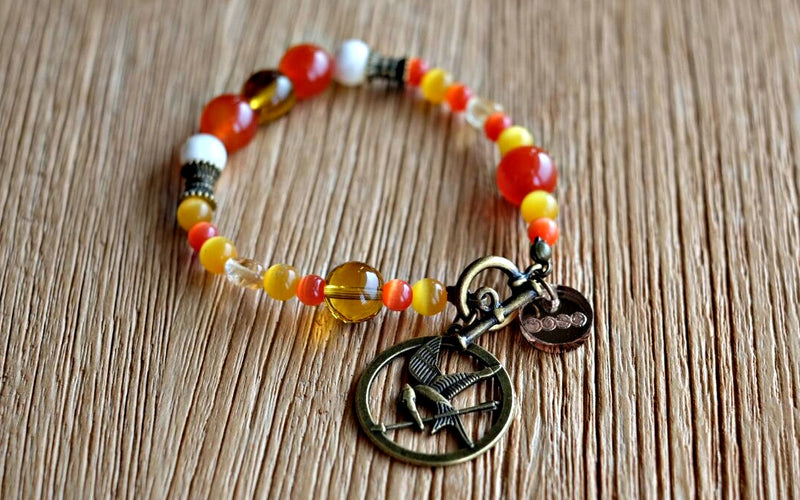 Orange- and golden-hued cat's eye, agate, manmade and natural citrine as well as seawater Mother of Pearl beads in varying sizes make up this Muse, to represent the fiery flames accompanying the Mockingjay charm.